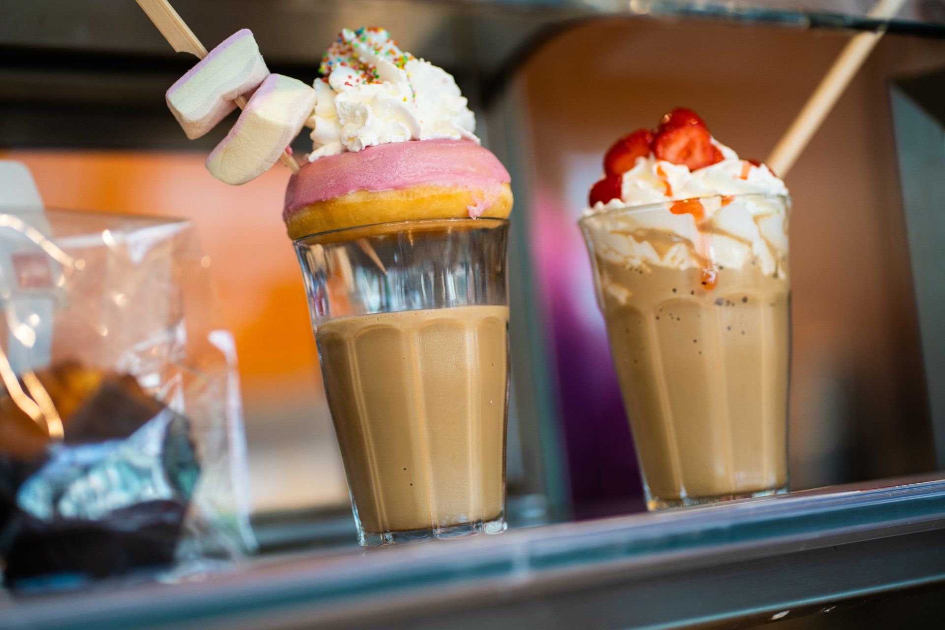 Op een plank staan twee milkshakes met slagroom en aardbeien.