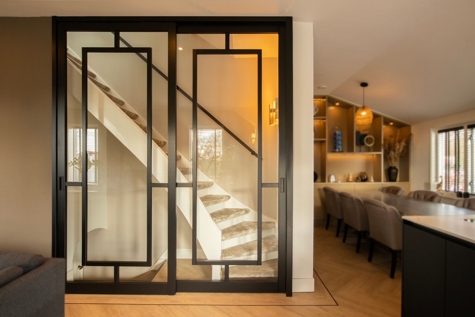 Door een glazen deur in een woonkamer is een trap zichtbaar.