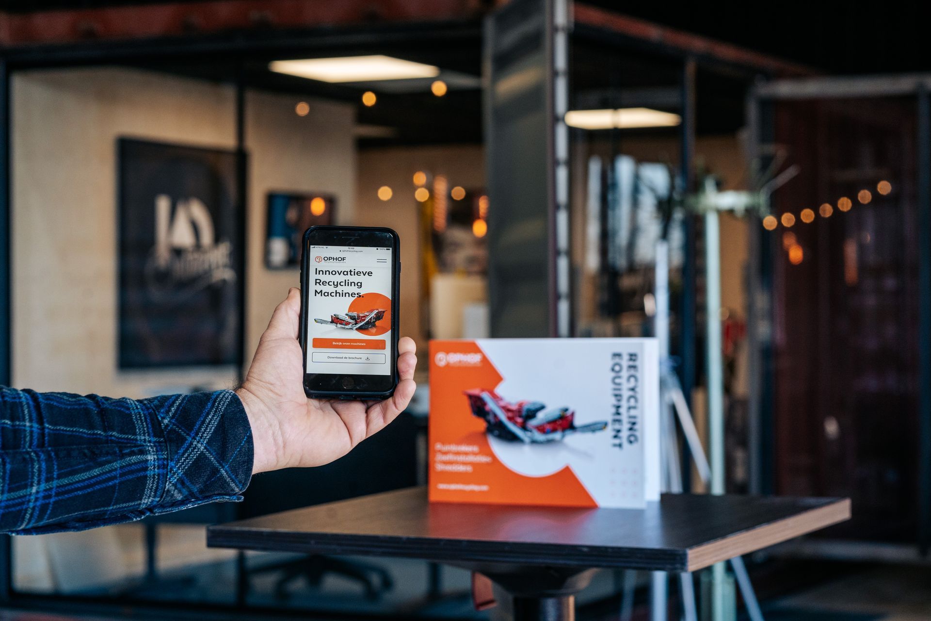 Een persoon houdt een mobiele telefoon in de hand voor een tafel.