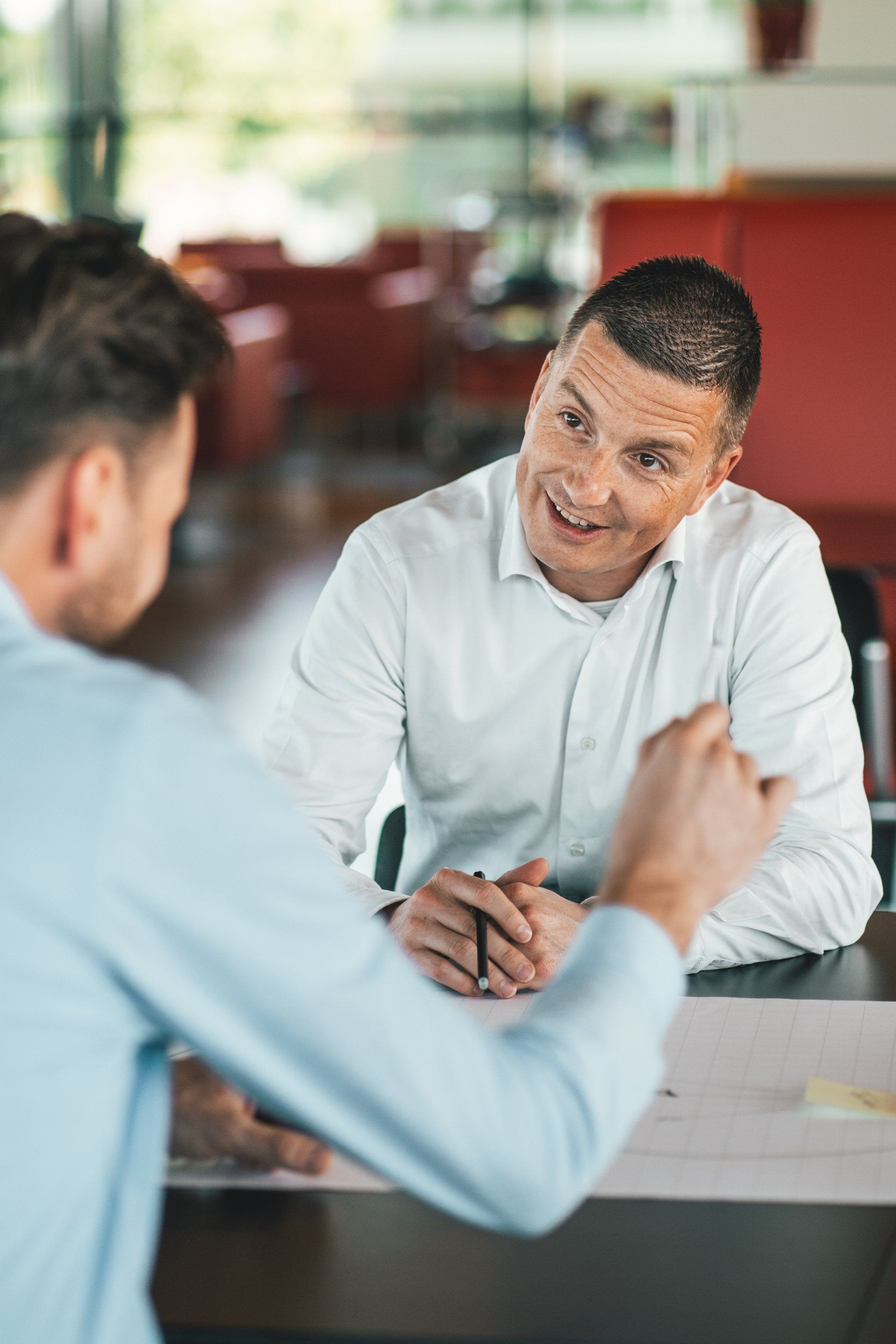 Twee mannen zitten aan een tafel en zijn met elkaar in gesprek.