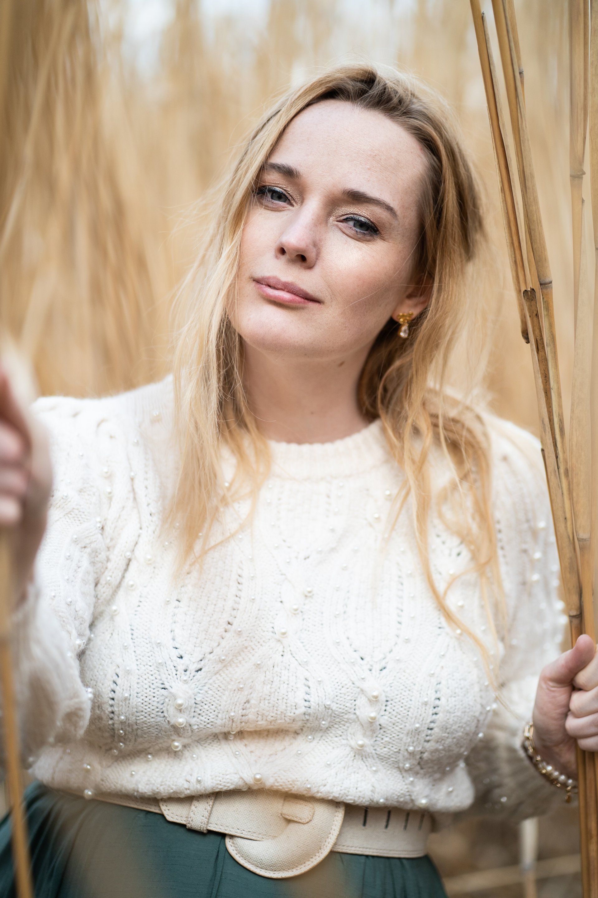 Een vrouw in een witte trui en groene rok staat voor een hek.