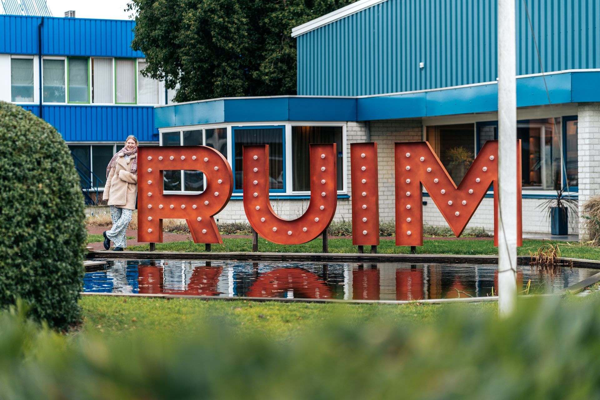 Voor een gebouw staat een groot rood bord met de tekst rum.