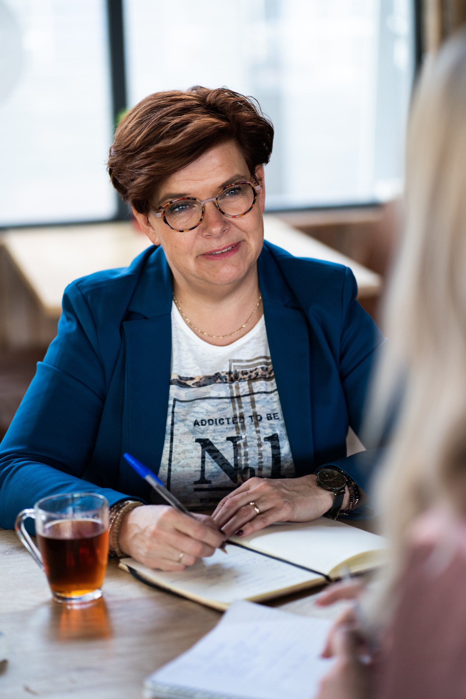 Een vrouw zit aan een tafel en schrijft in een notitieboekje.