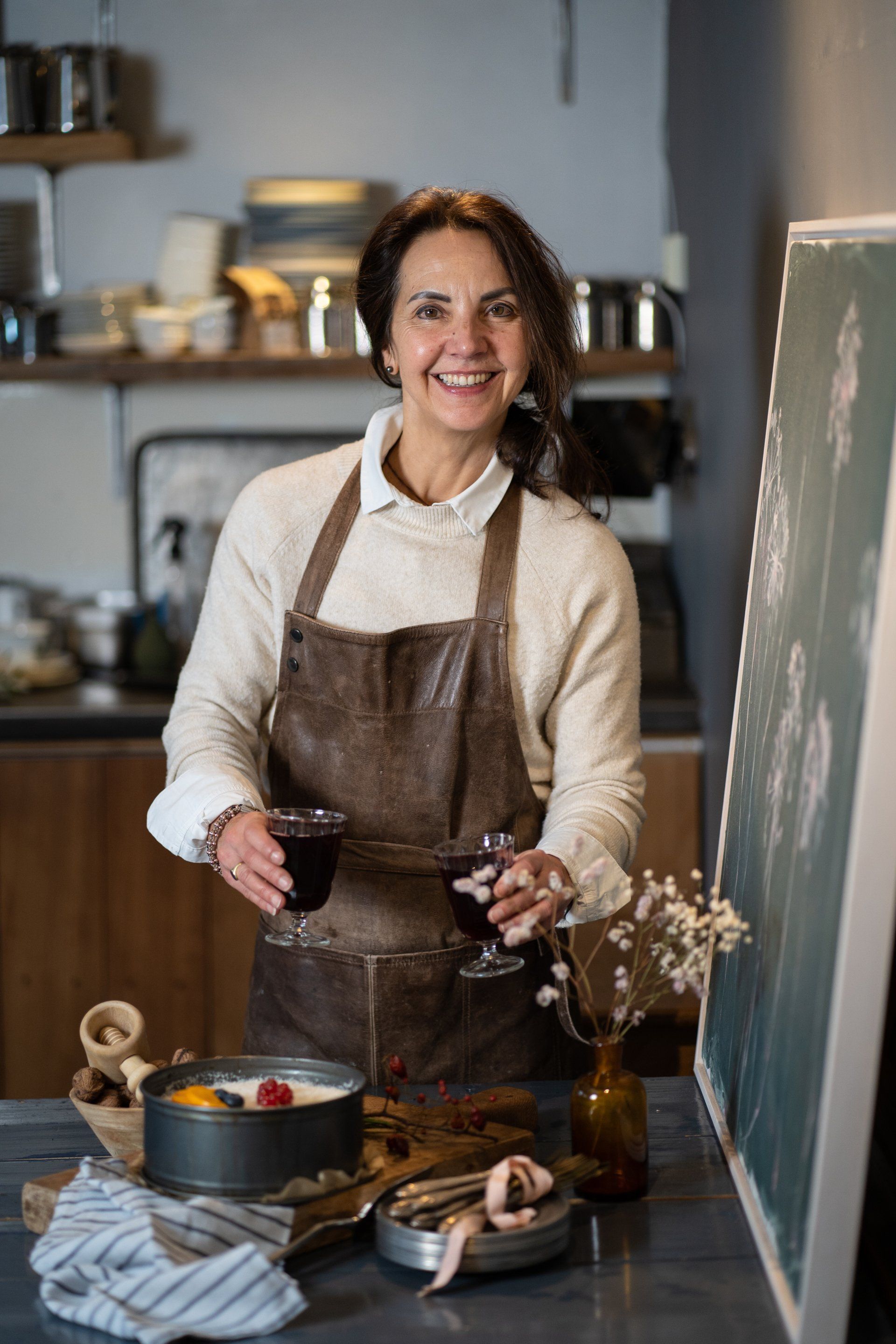 Een vrouw in een schort houdt een glas wijn vast in een keuken.
