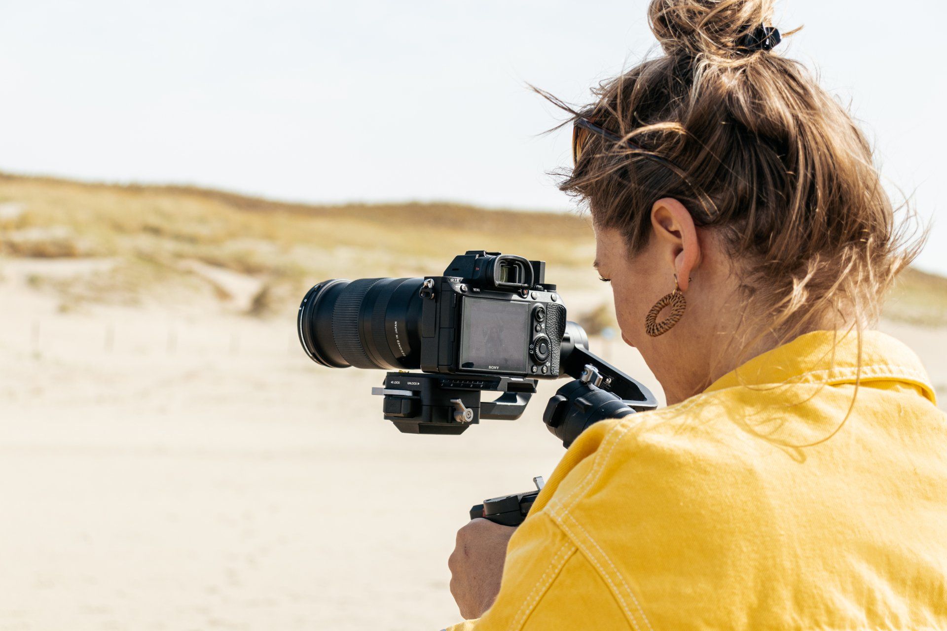 Een vrouw in een geel jasje houdt een camera op een statief vast.