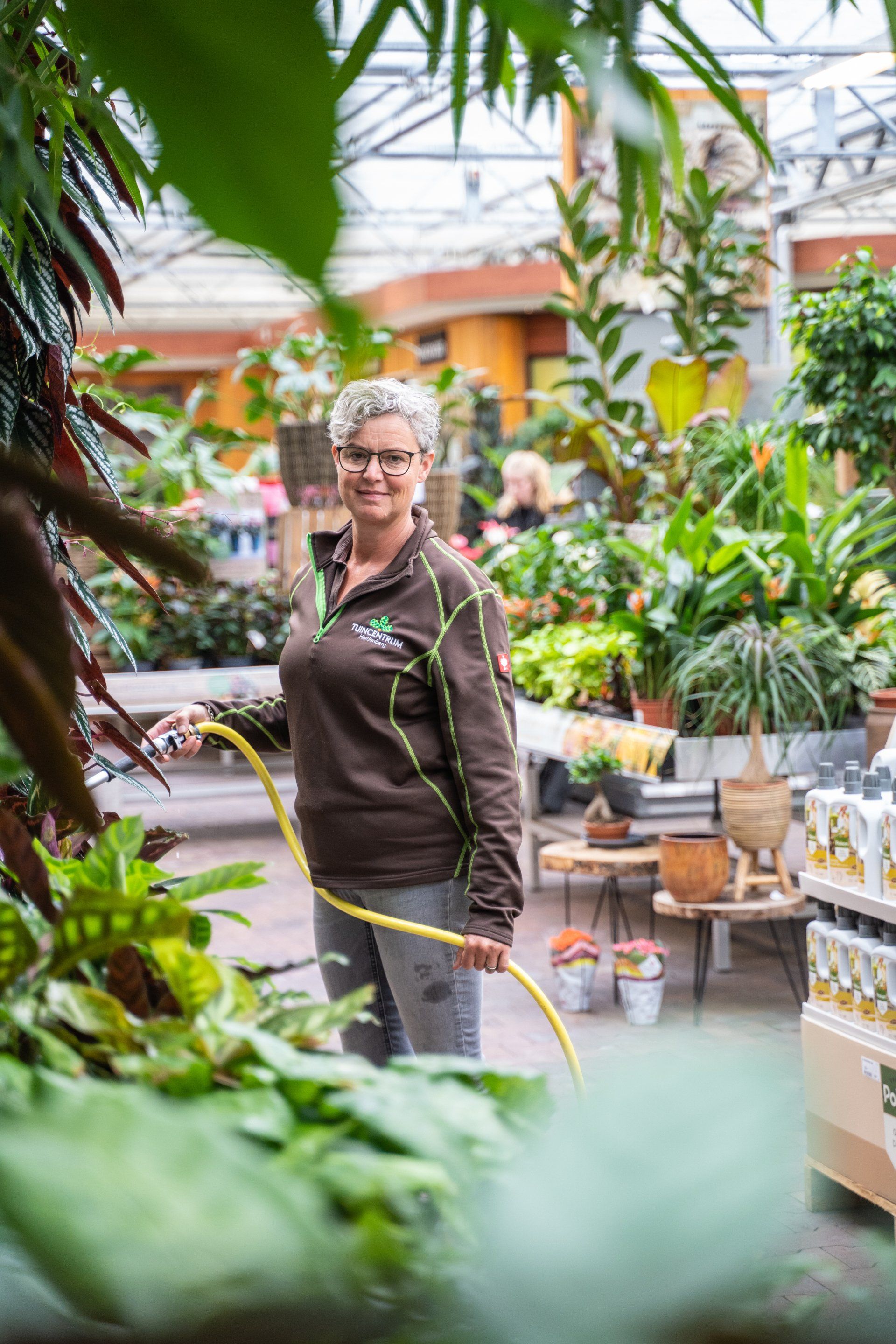 Een vrouw geeft met een slang planten water in een kas.