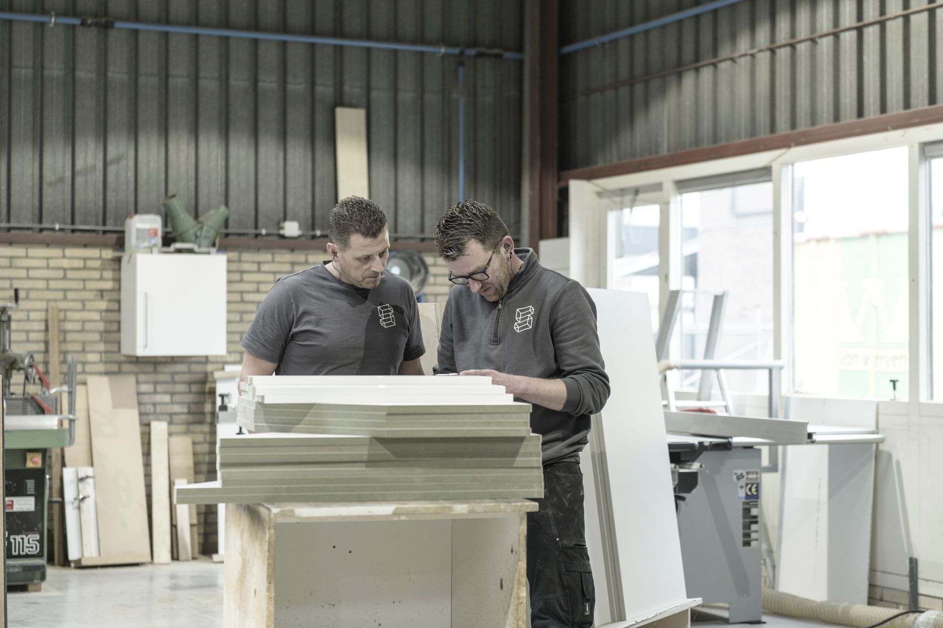 Twee mannen staan ​​in een werkplaats naast elkaar en kijken naar een stuk hout.