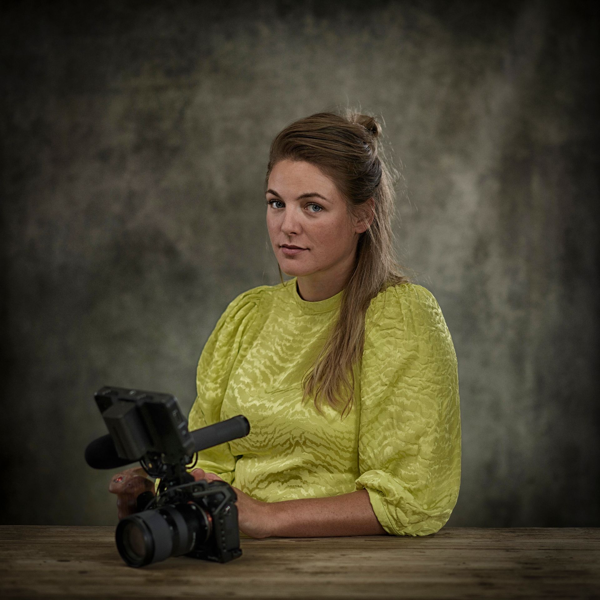 Simone zit aan een tafel en houdt een camera vast.