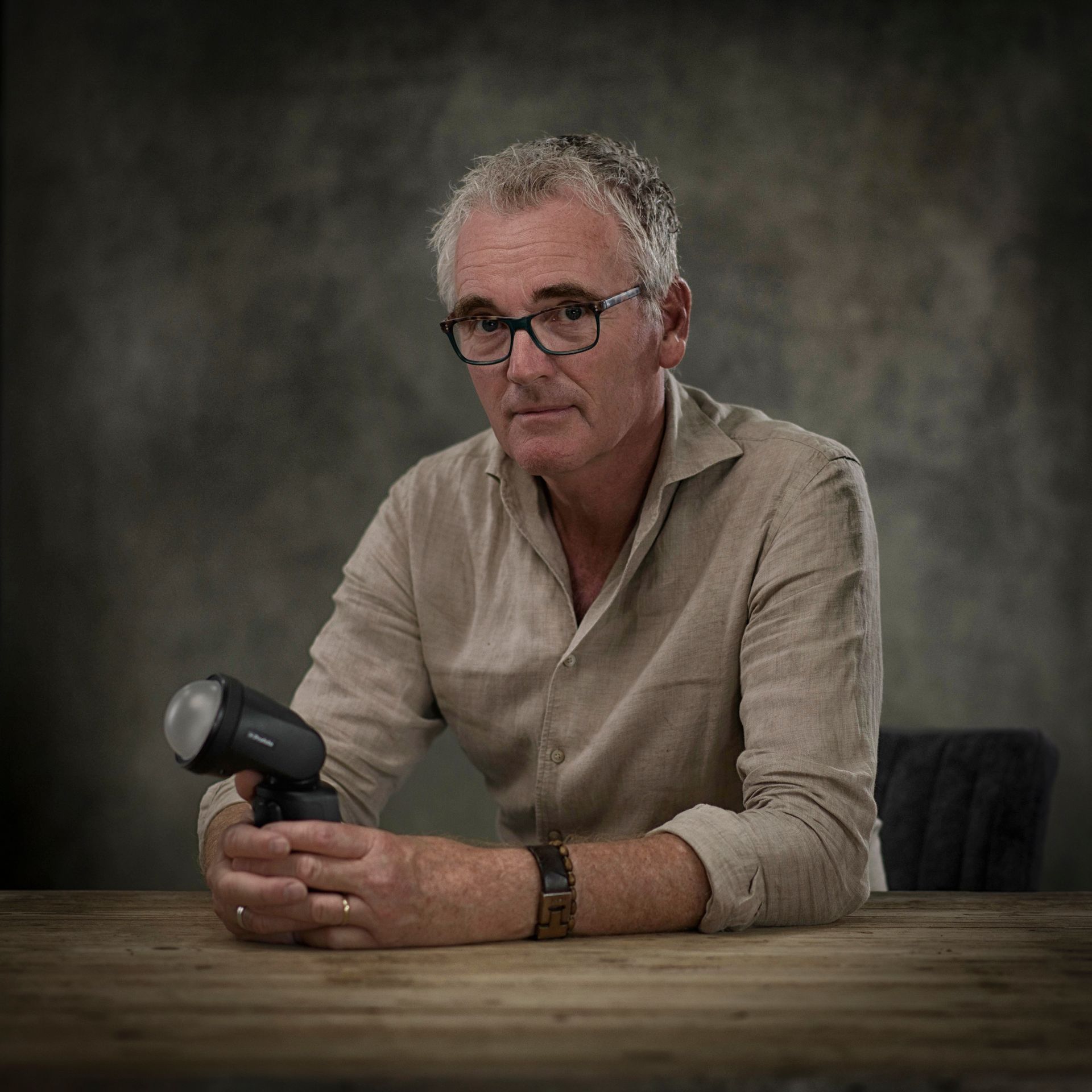 Een man met een bril zit aan een tafel en houdt een zaklamp vast.