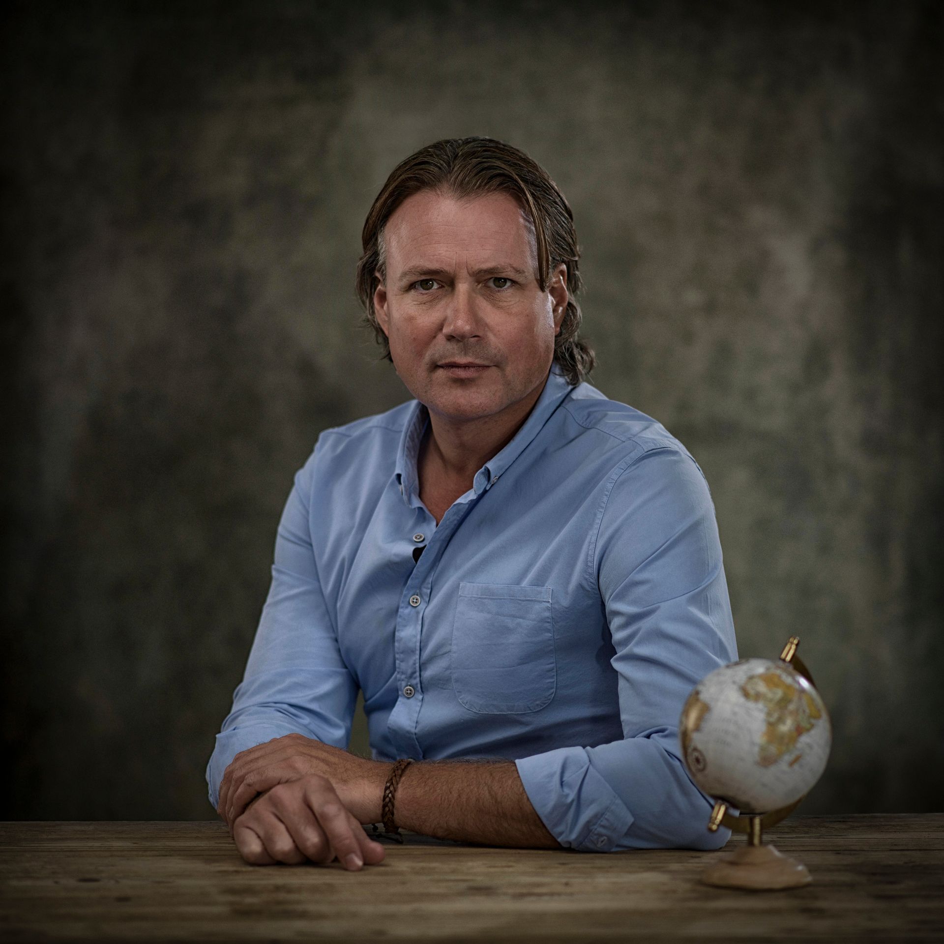 Een man in een blauw shirt zit aan een tafel naast een wereldbol.