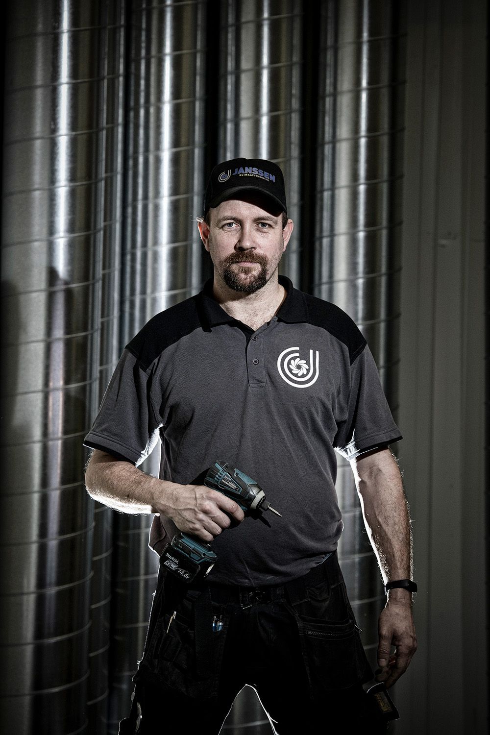 Voor een muur staat een man met een boormachine in zijn hand.