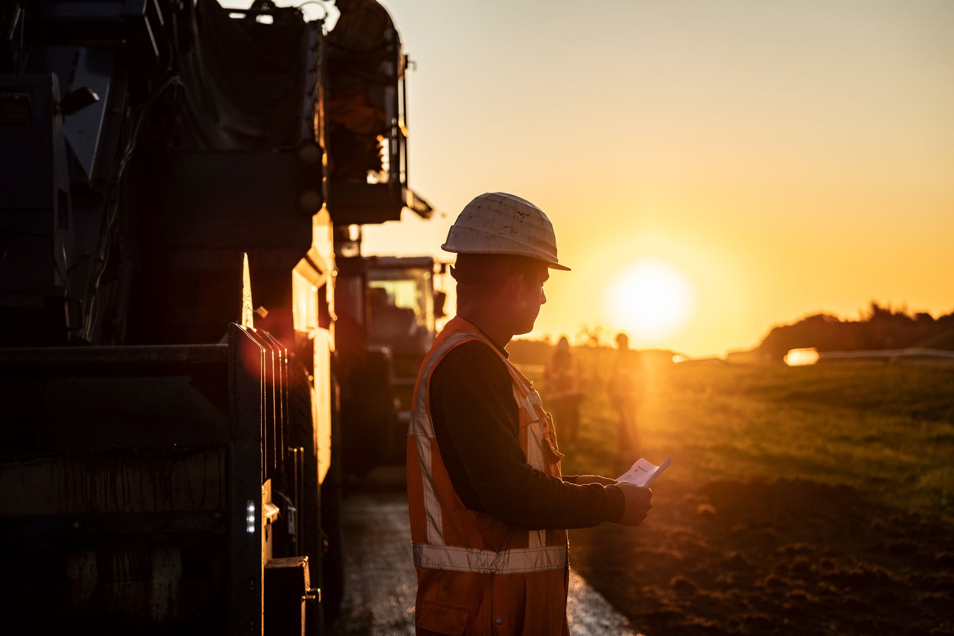 Een bouwvakker staat bij zonsondergang voor een kraan.