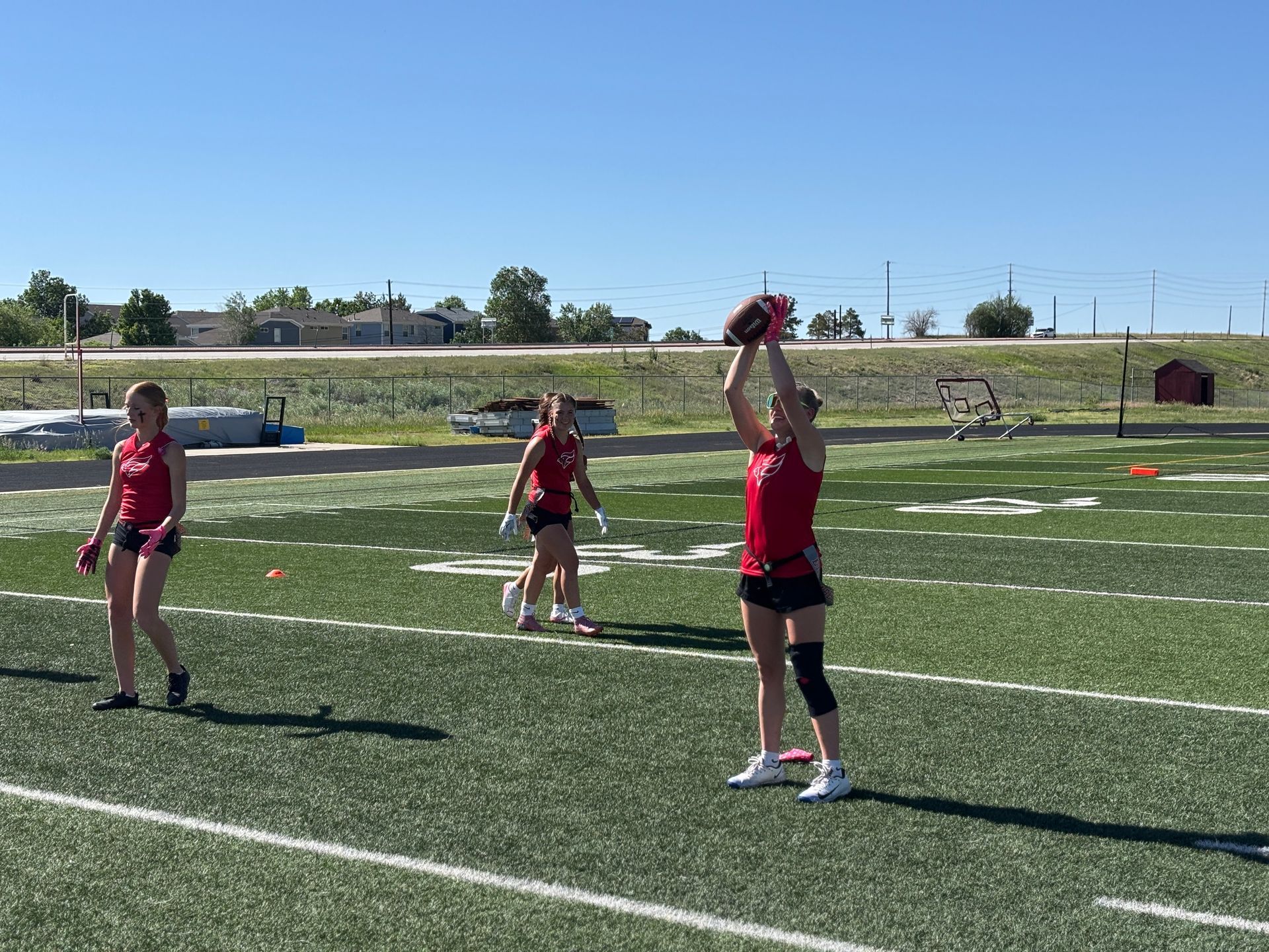 Kids in red jerseys playing catch on a football field under a clear blue sky