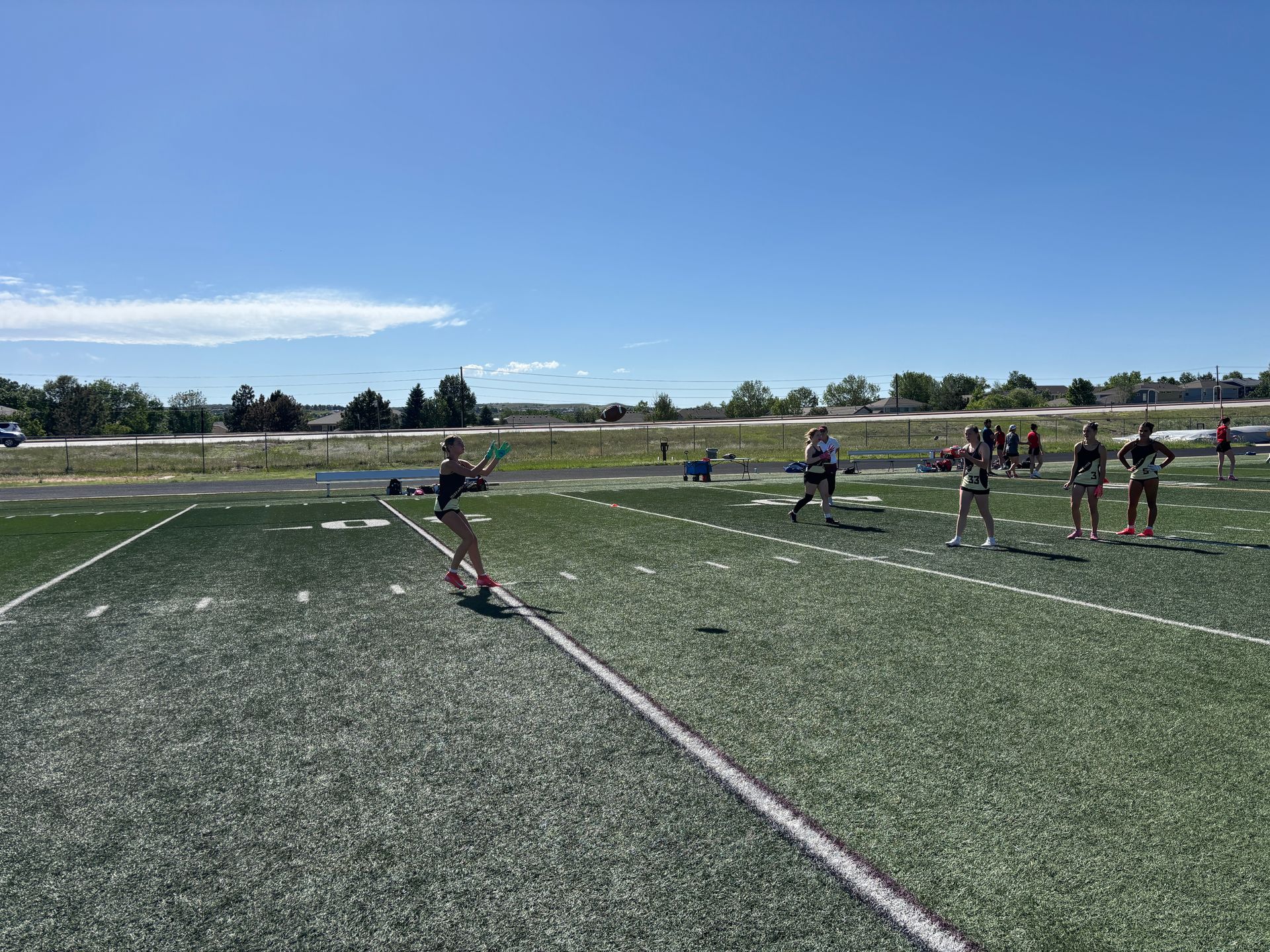 Flag football players lined up on a sunny turf field under a clear blue sky.