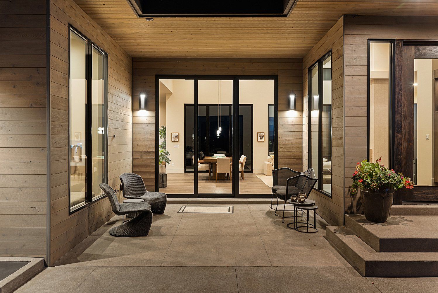 A patio with chairs and a table in front of a house with sliding glass doors.