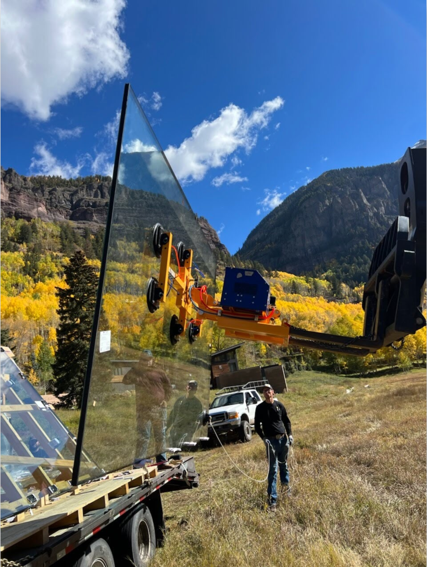 A man is standing in a field looking at a large piece of glass being lifted by a crane.