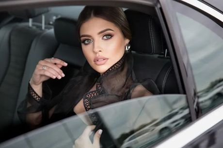 A woman in a black dress is sitting in the back seat of a car.