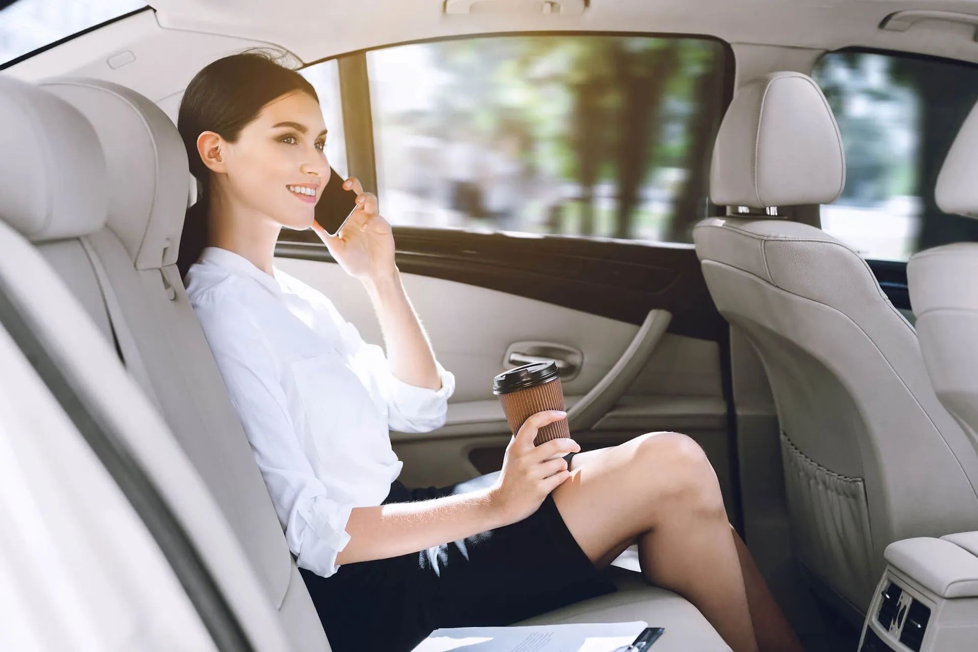 A woman is sitting in the back seat of a car talking on a cell phone.