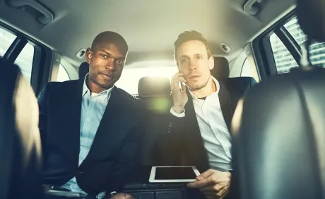 Two men in suits are sitting in the back seat of a car.