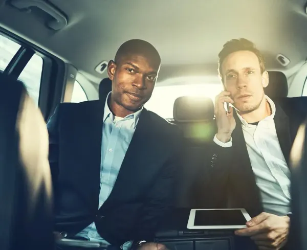 Two men in suits are sitting in the back seat of a car.
