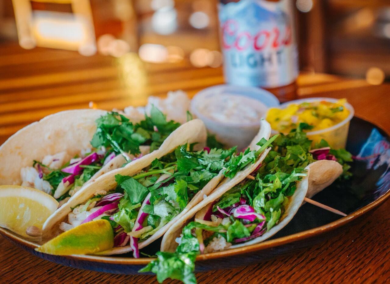 Plate of fish tacos with cilantro, slaw, lime, mango salsa, and beer.