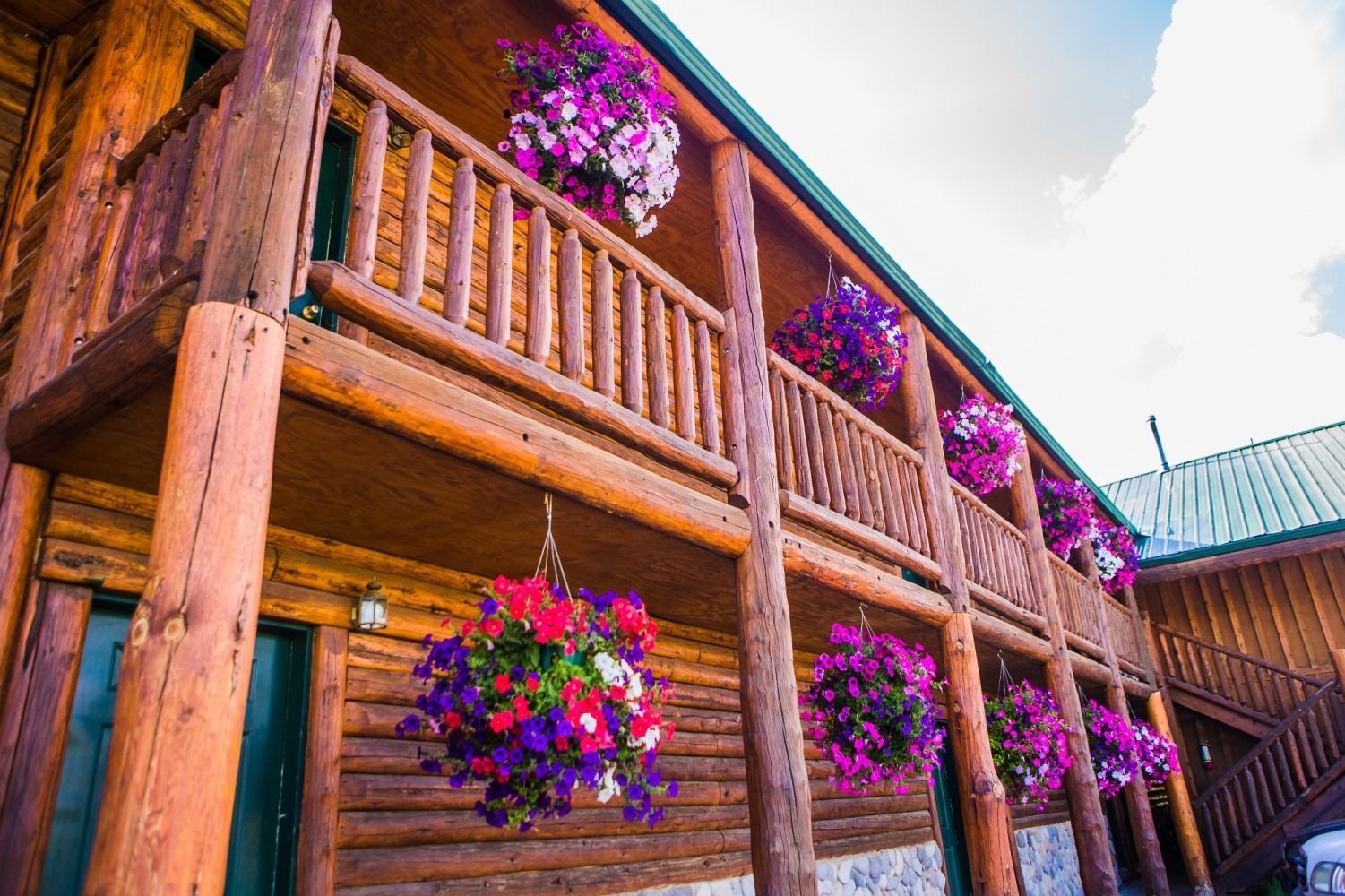 Log cabin with a balcony lined with hanging flower baskets in various colors.