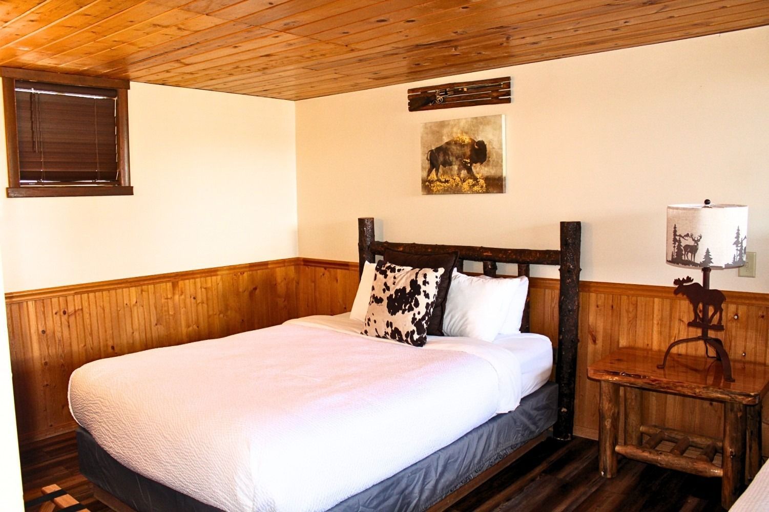 Bedroom with a double bed, wooden paneling, ceiling, and nightstand with a lamp.