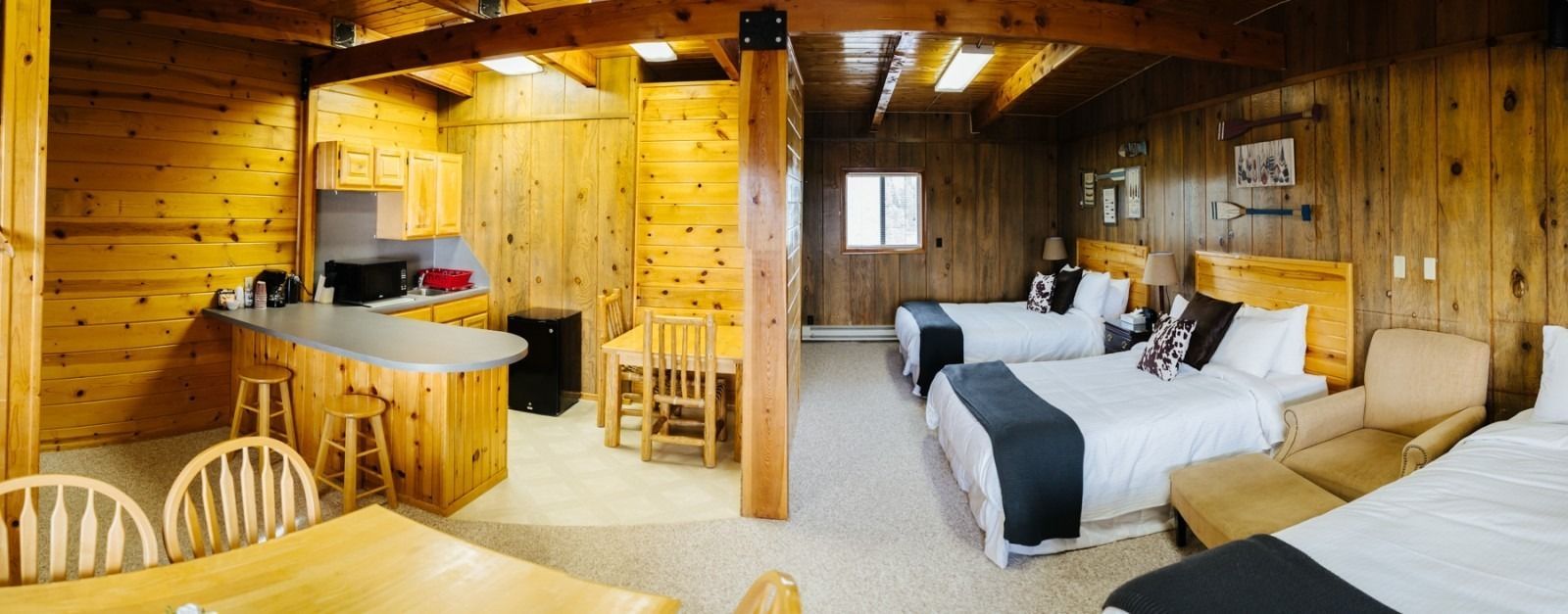 Interior view of a rustic cabin with wooden walls, featuring a kitchen area and multiple beds.