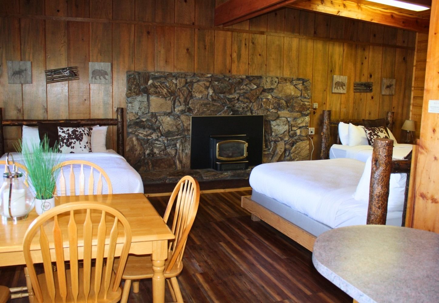 Rustic cabin interior with stone fireplace, two beds, dining table, and wood paneling.