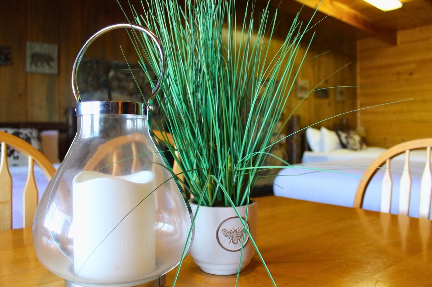 Wooden table with a lantern, plant in a pot, and a bed in a wood-paneled room.