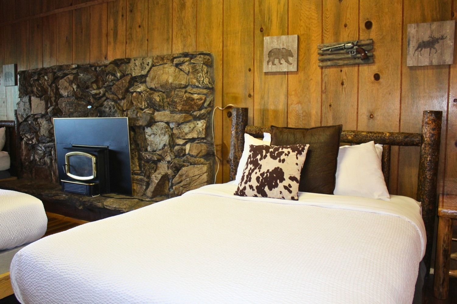 Bedroom with rustic wood paneling, stone fireplace, and double bed with decorative pillows.