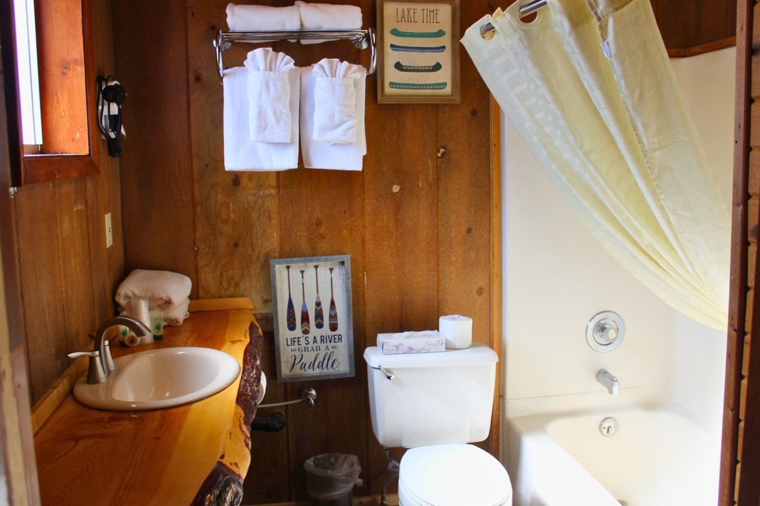 Small bathroom with wood paneling, white fixtures, towels, and a shower curtain.