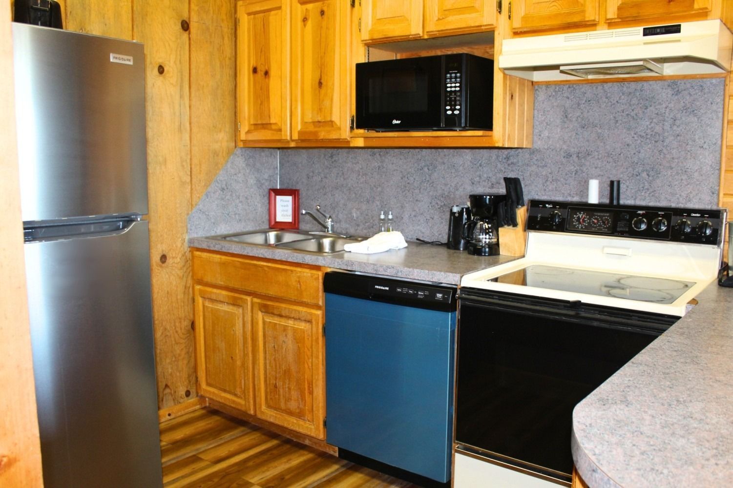 Kitchen with stainless steel refrigerator, wooden cabinets, blue dishwasher, and black oven.