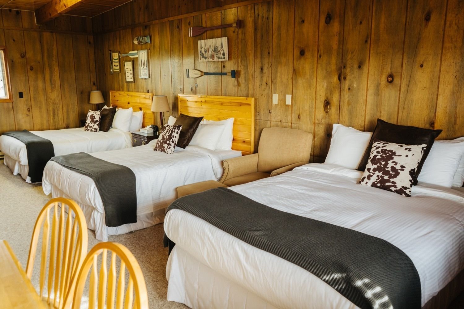 Bedroom with three beds, wooden walls, neutral bedding, and decorative pillows.
