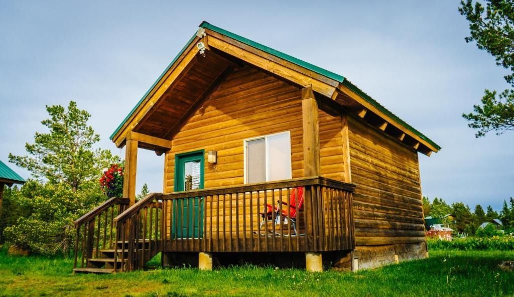 Wooden cabin with porch, green door, and dark green roof, set in grassy area.
