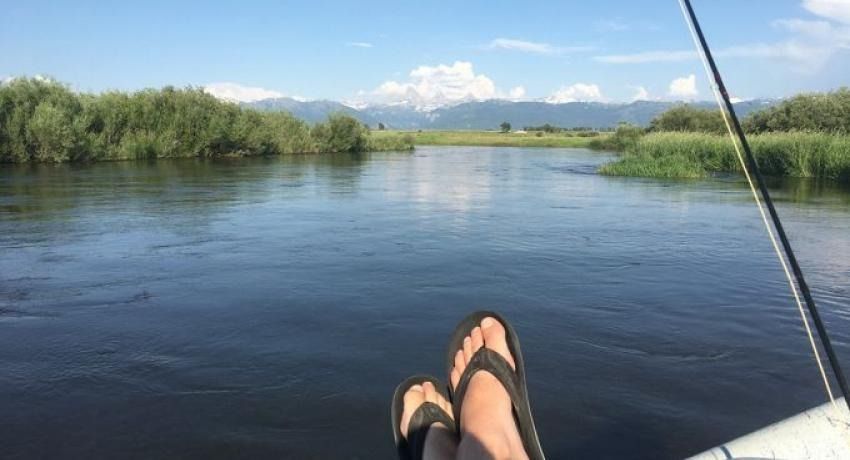Person relaxing on a boat, feet up, on a river with mountains in the background.