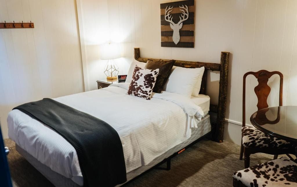 Bedroom with a wooden bed, white bedding, cowhide pillow, and rustic art.