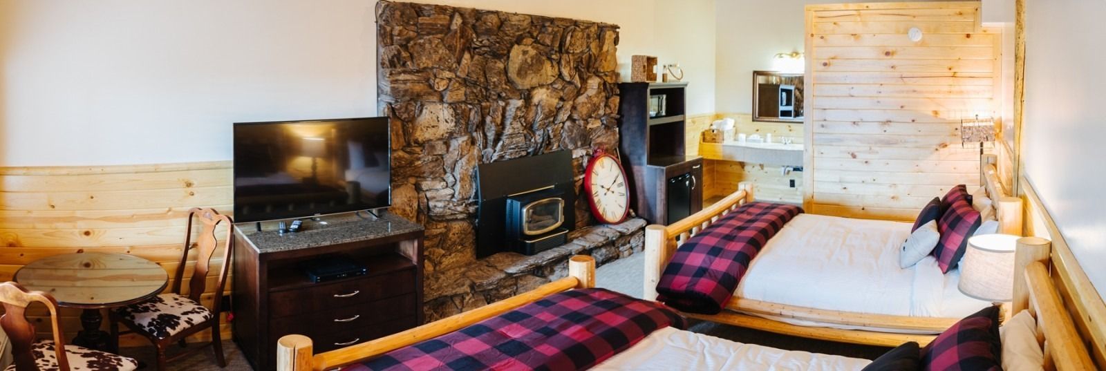 Rustic bedroom with stone fireplace, two beds with plaid blankets, and wooden walls.
