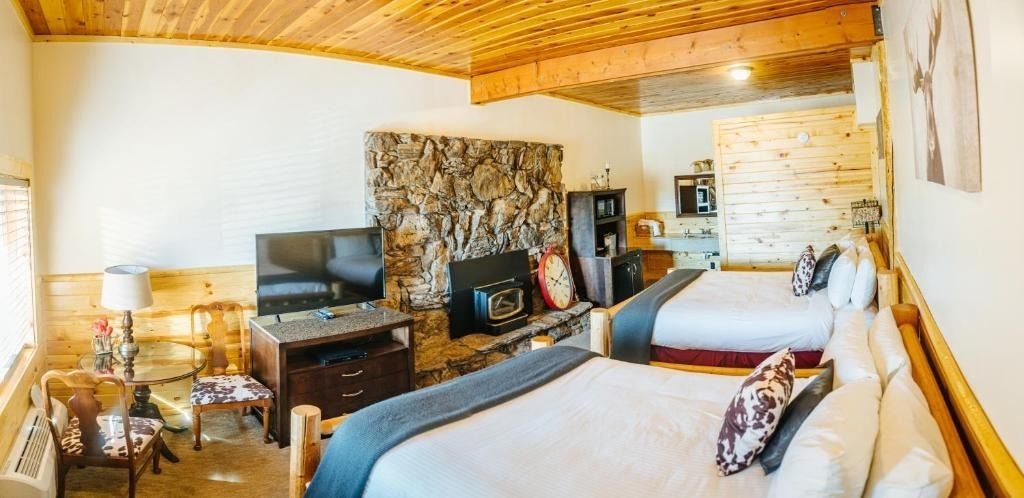 A hotel room with two beds, a stone fireplace, and a wooden ceiling.