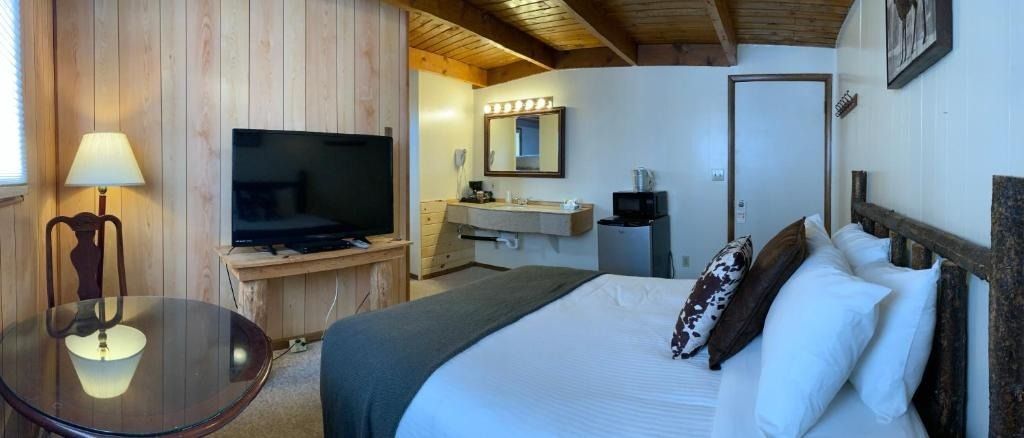 Bedroom with a bed, TV, table, and bathroom. White and brown color scheme.