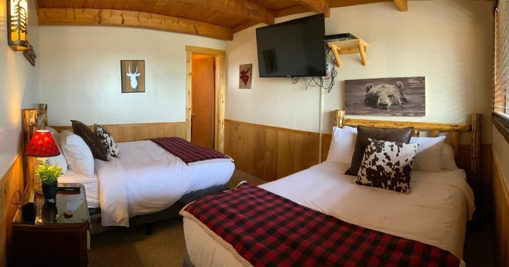 A rustic bedroom with two double beds, wooden walls, a TV, and artwork.