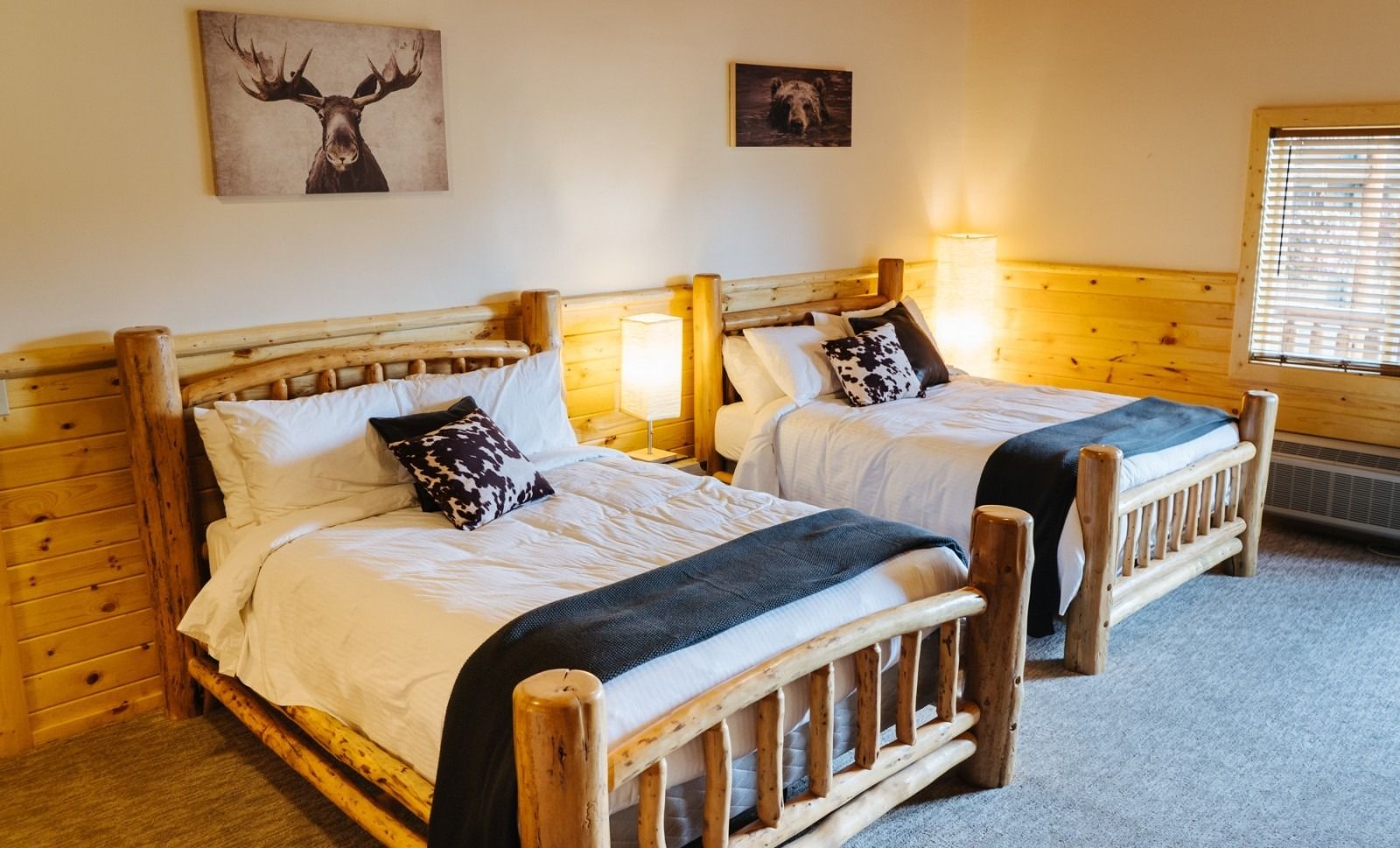 Two beds in a rustic wood-paneled hotel room with animal artwork on the walls.