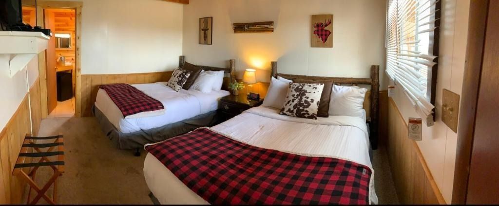 A rustic hotel room with two double beds, plaid blankets, and wooden furniture.