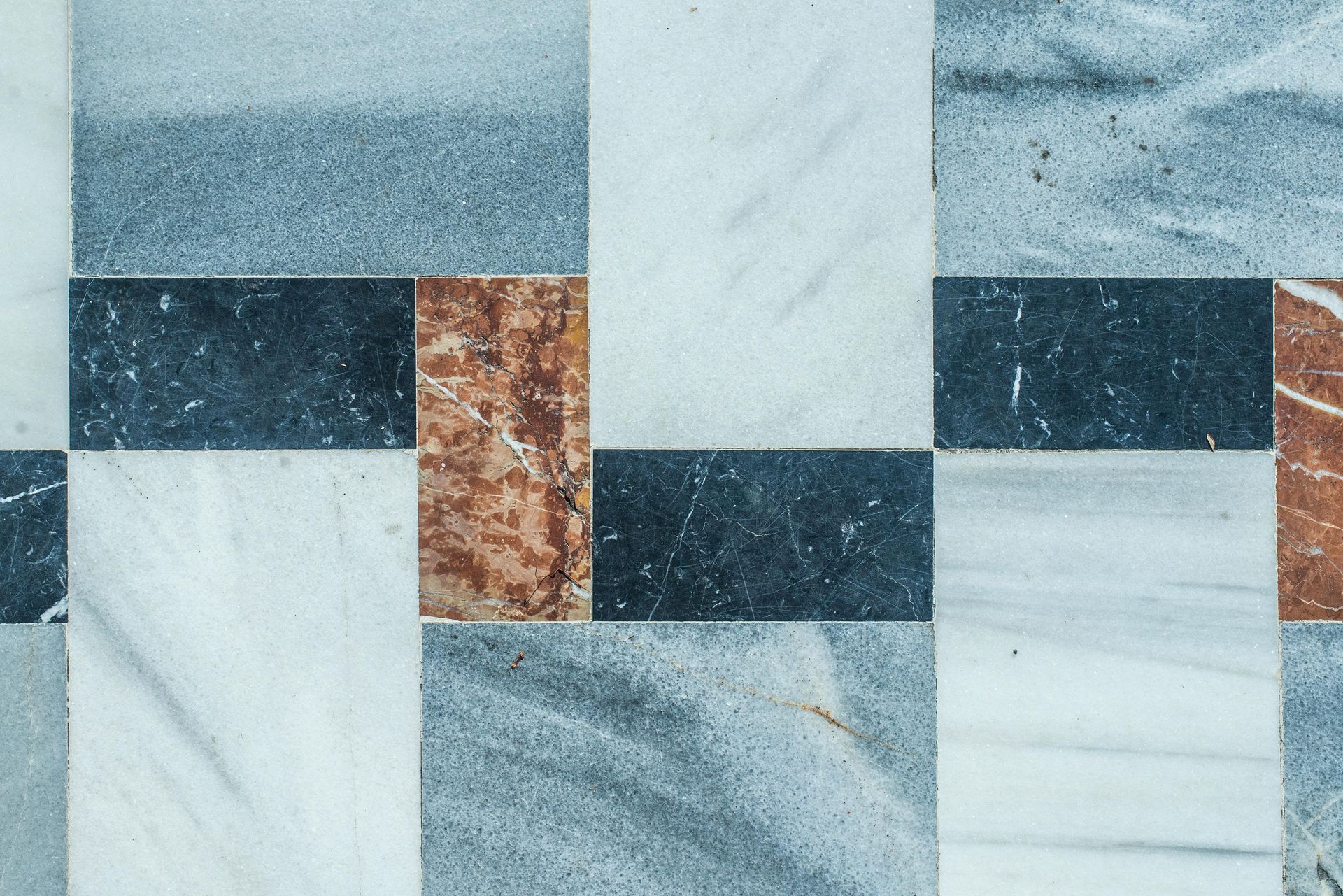 Close-up of a tiled floor with rectangular blocks in various colors and textures, including white, blue, black, and rust.
