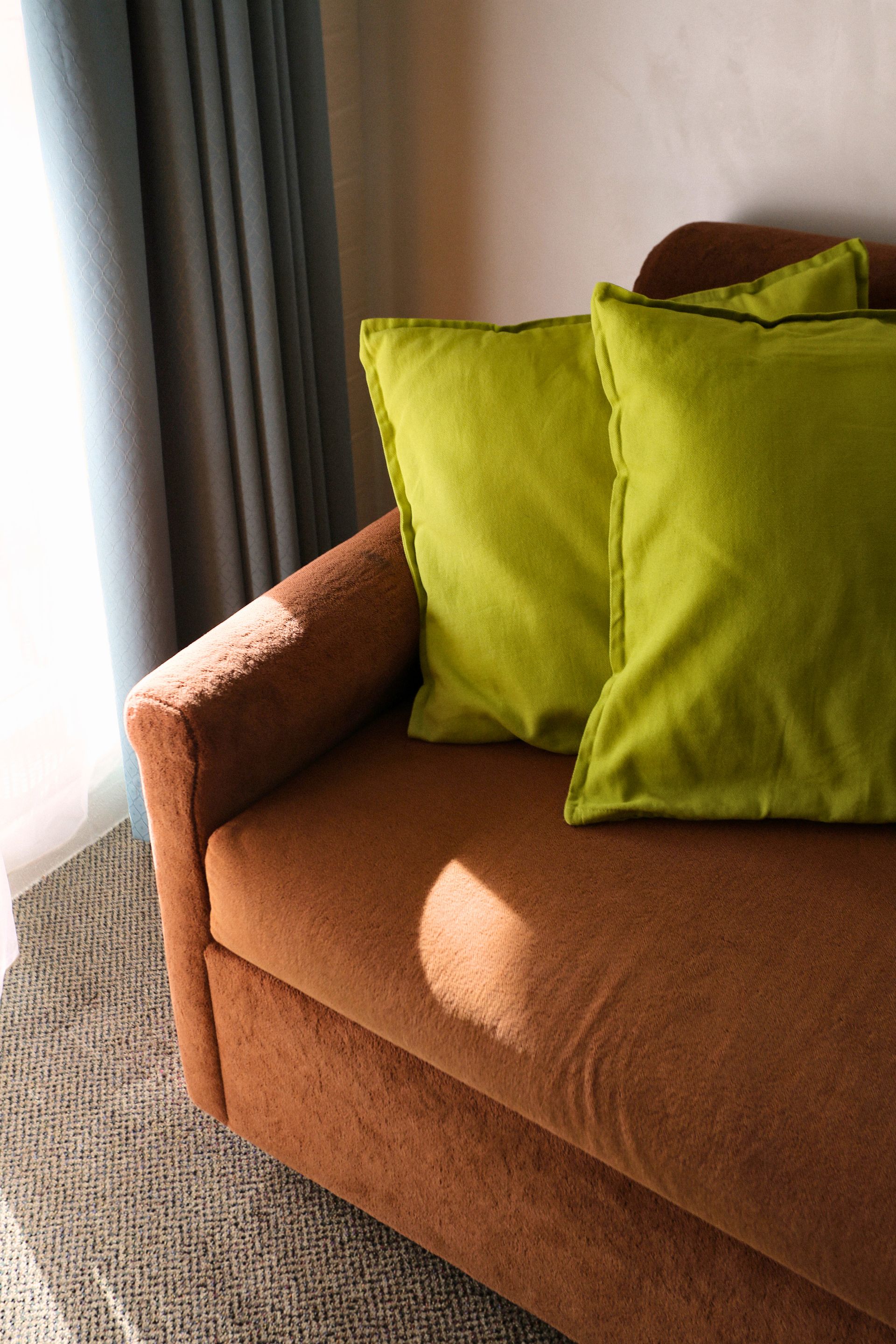 Brown sofa with two green pillows near a window with blue curtains.