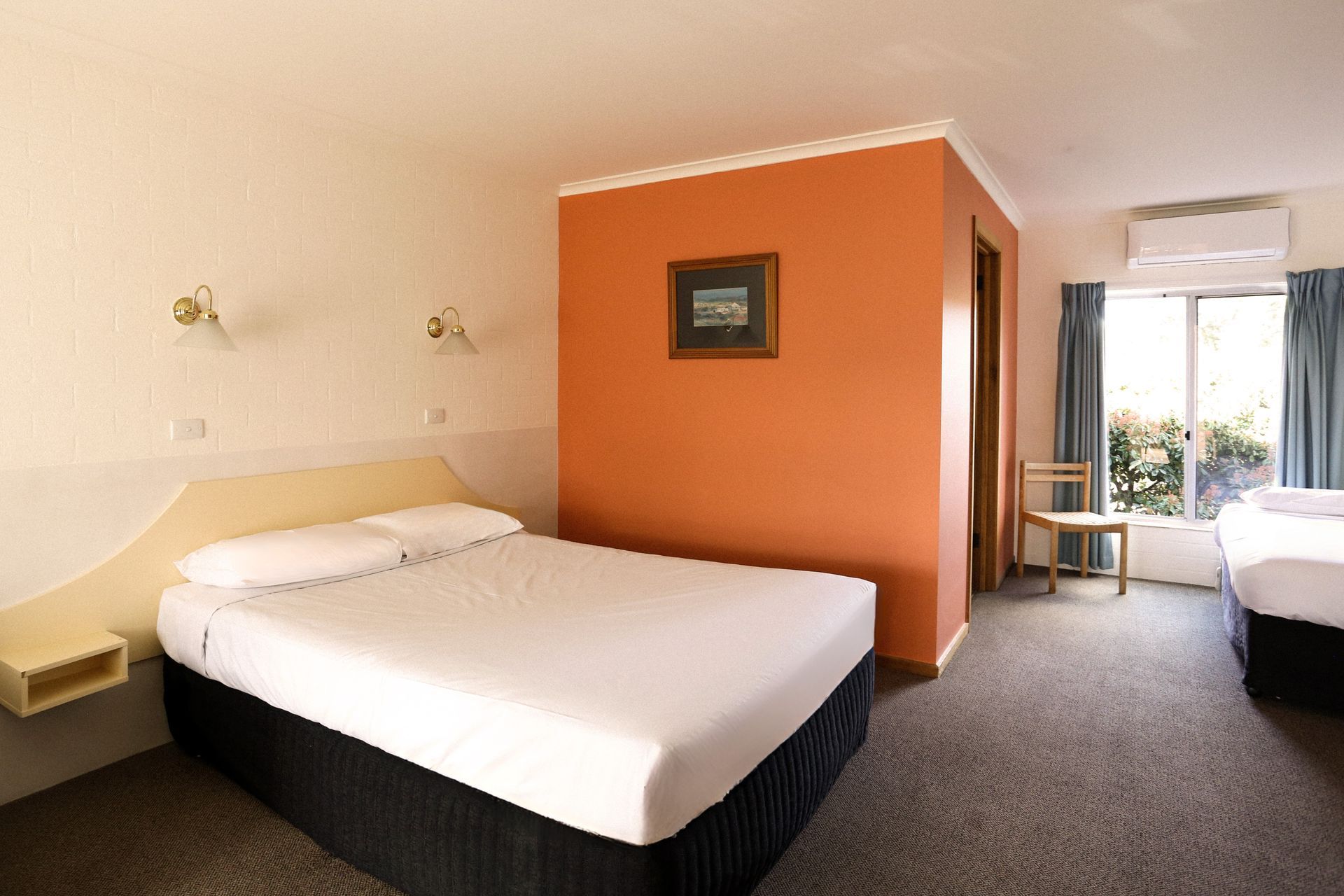 Motel room with a bed, orange accent wall, and a window.