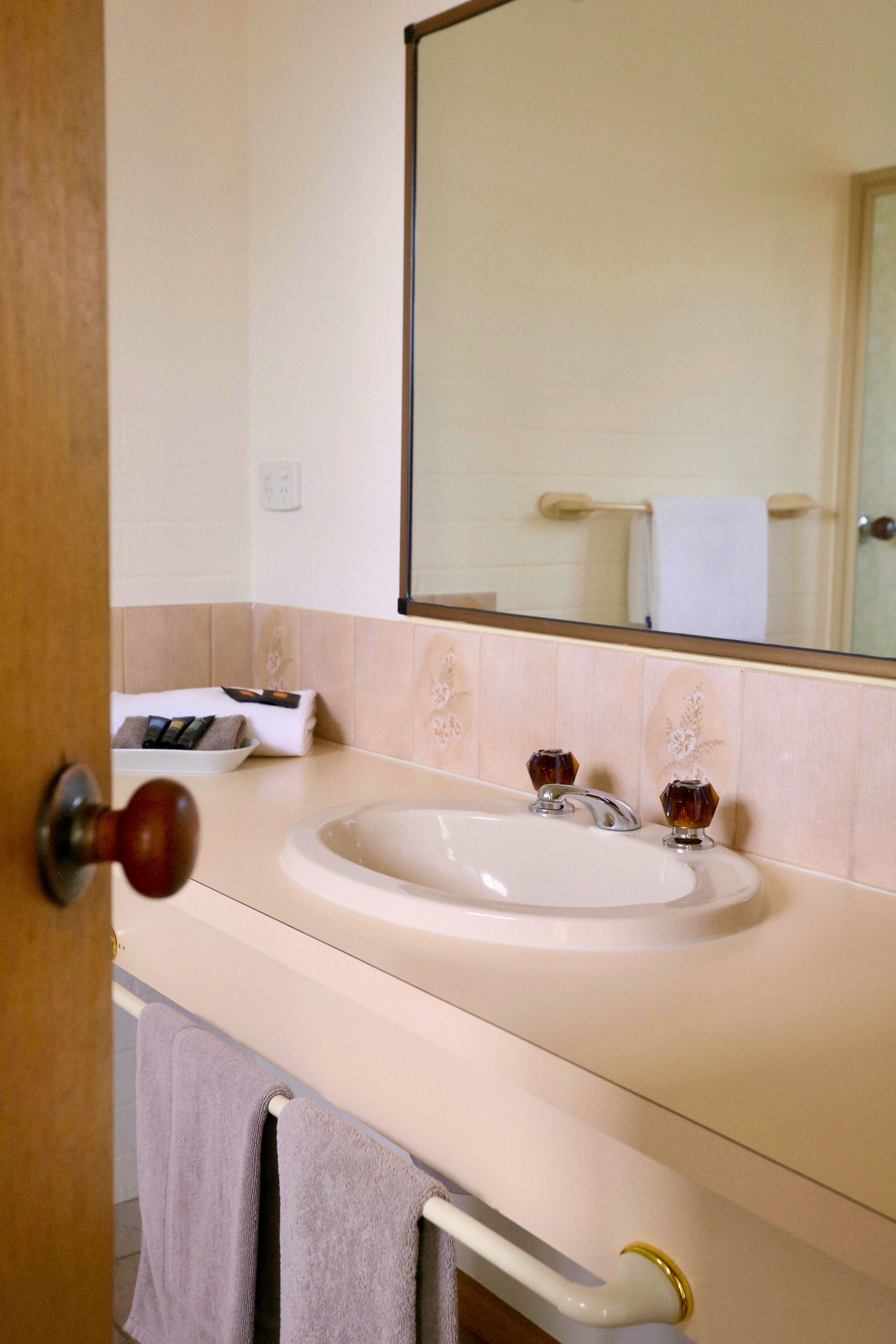 Bathroom sink with a mirror. Tan countertop with a white sink. Towels hanging below.