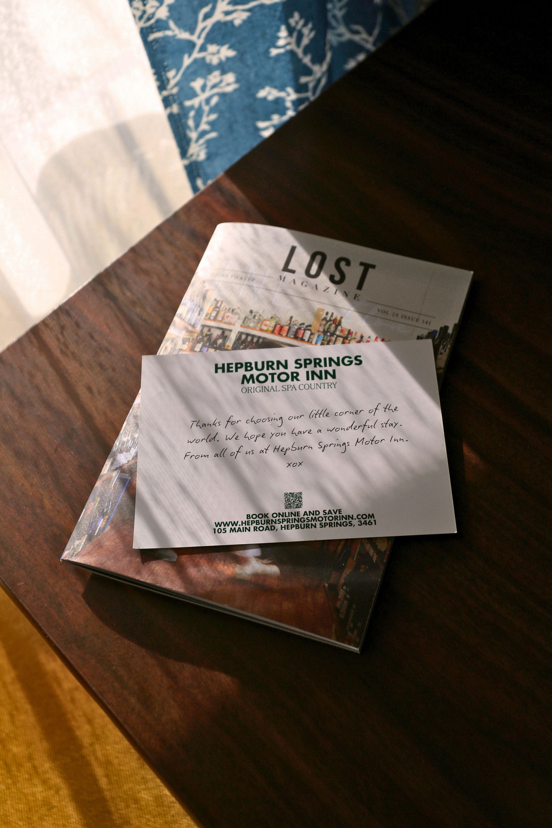 A hotel brochure and a note from the Hidden Springs Motor Inn on a wooden table, bathed in sunlight.