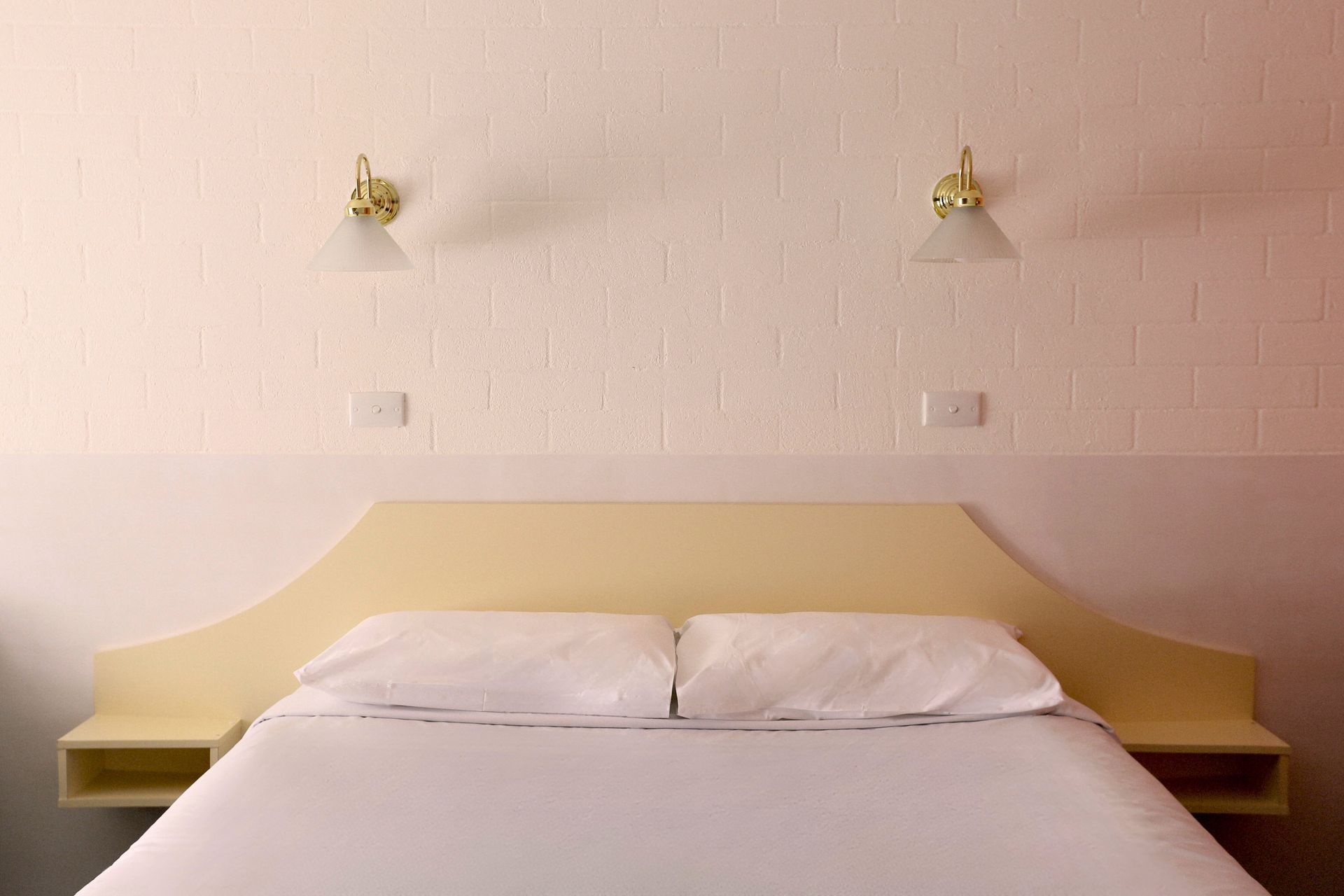 Bedroom with double bed, cream headboard, white sheets, two bedside tables, sconces on textured wall.