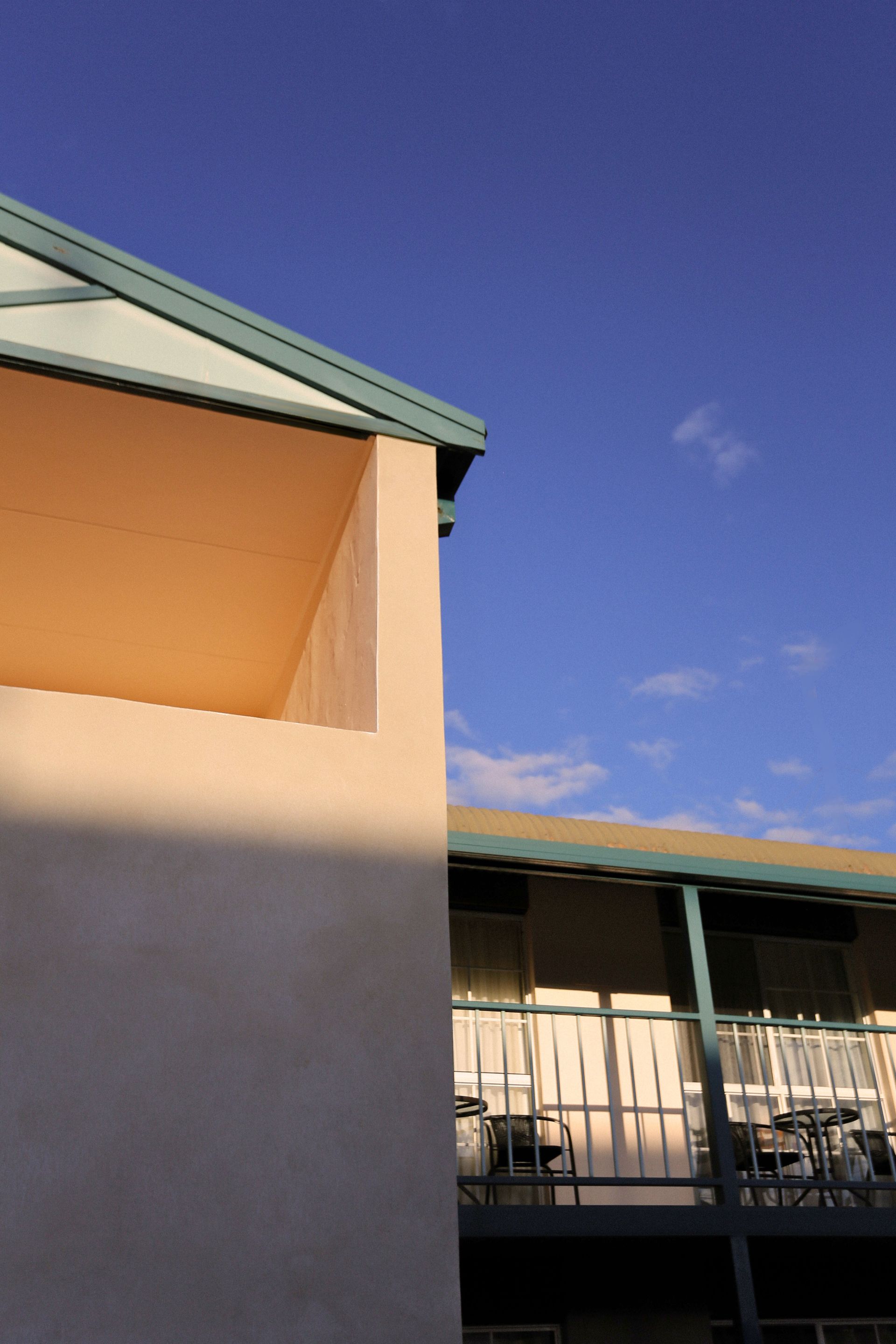 Beige building corner with teal trim against a bright blue sky.